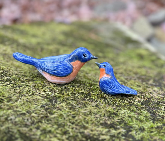 Two blue bird figurines on a mossy surface
